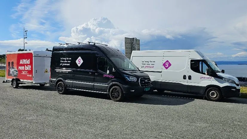 To utleiebiler fra med getaround profilering parkert ved sjøen, den ene med henger som reklamerer for bilvask.