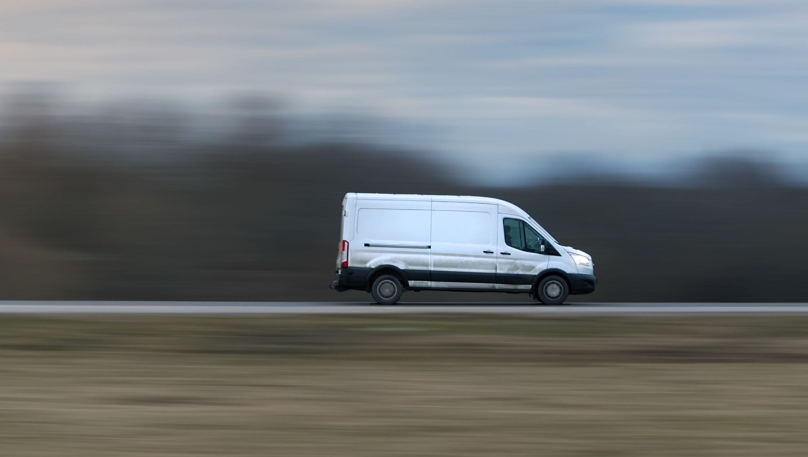 Hvit varebil i høy fart på motorvei, med uskarp bakgrunn som viser bevegelse.