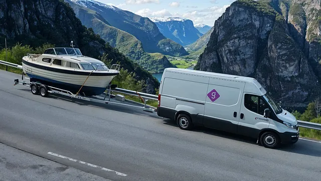 Hvit varebil trekker en fritidsbåt på henger opp en fjellvei med bratte fjellsider og grønn dal i bakgrunnen.